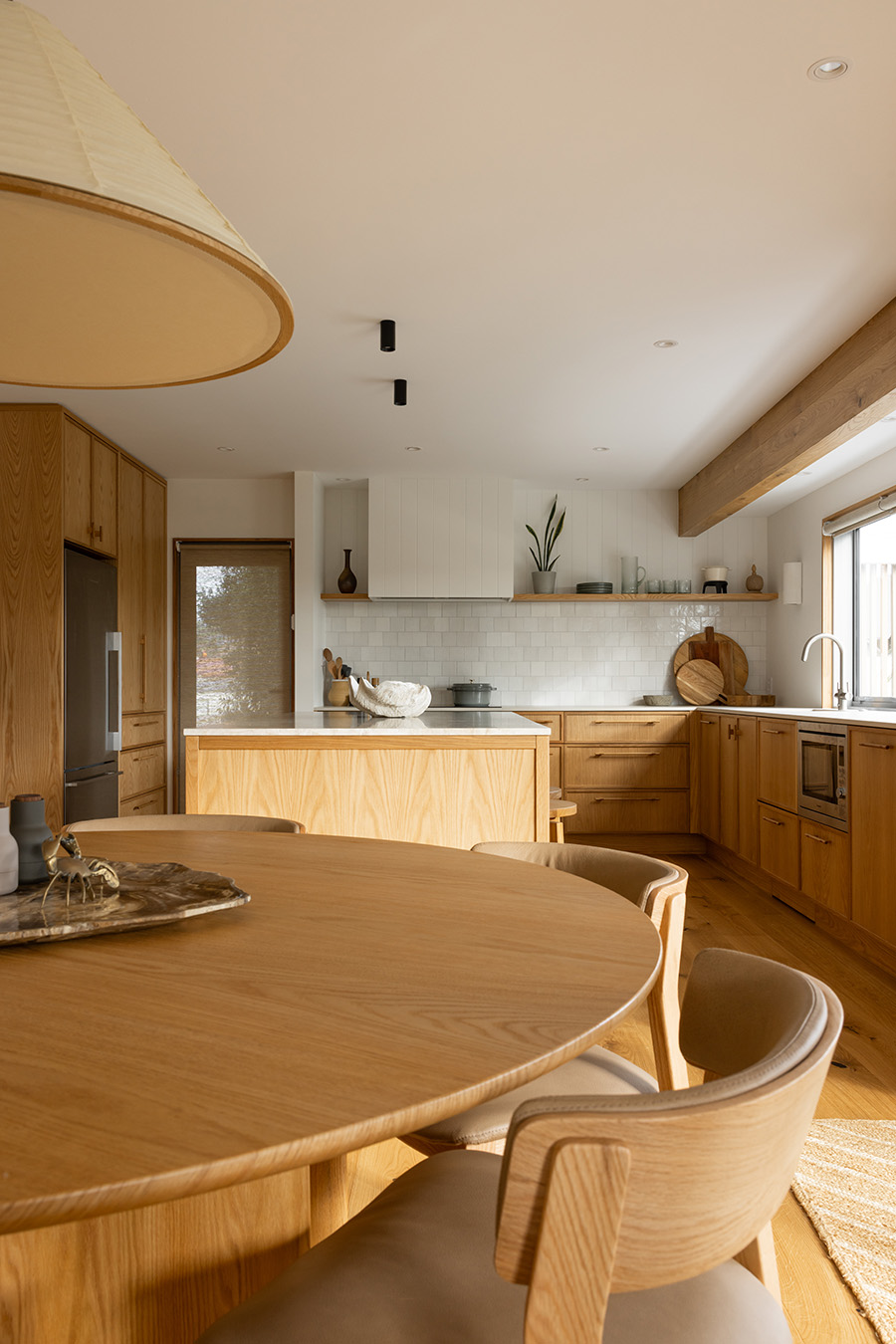 Japandi-style kitchen and dining area with round timber table and woven chairs. Coastal interior design.