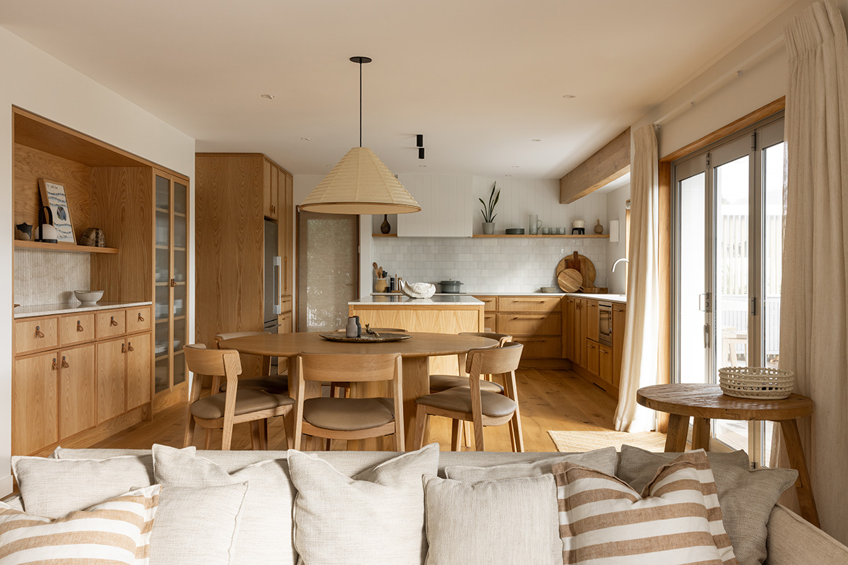 Open-plan living and dining space in a coastal home with timber dining furniture and coastal kitchen joinery.