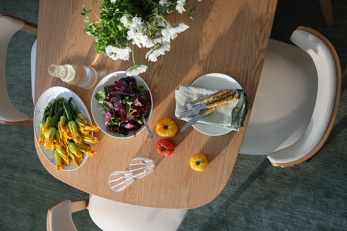 Spring table setting from above with fresh florals and fruits, zucchini flowers and a green salad on oak table.