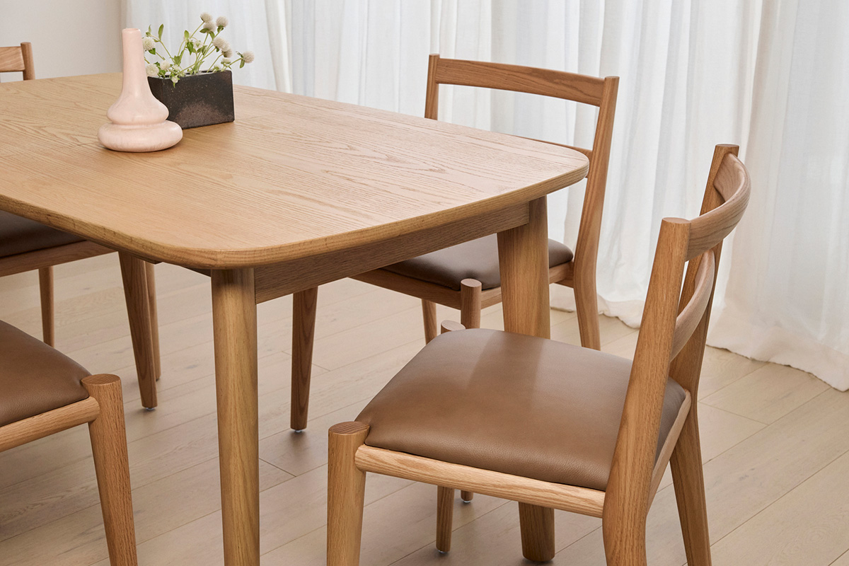 A timber dining setting in natural oak, styled minimally in a modern dining room framed by flowing drapery.